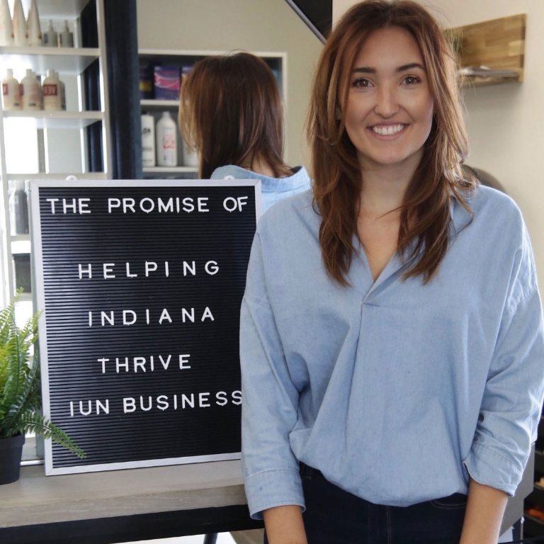 Danielle Roeske poses in front of a sign that says, "The promise of helping Indiana thrive."