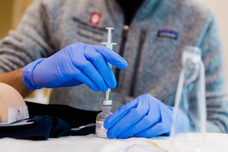 Hands in blue gloves use a syringe to draw the COVID-19 vaccine from a vial