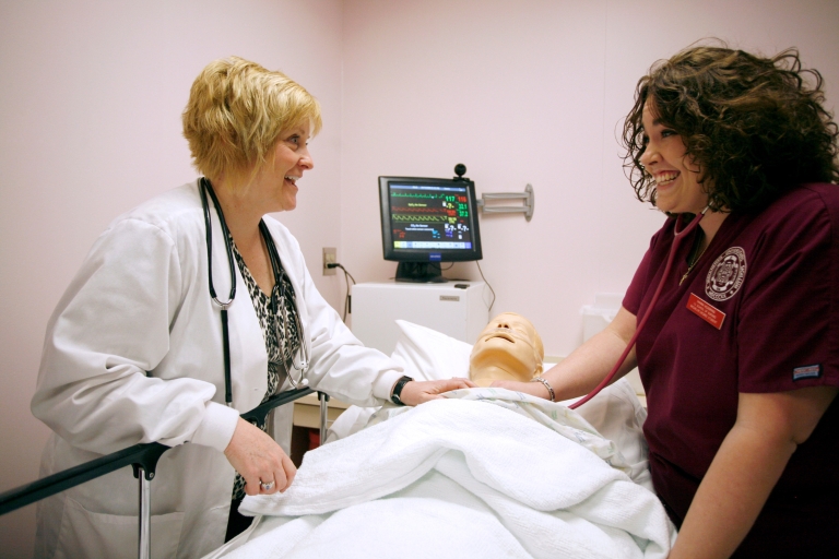 Health sciences faculty member and student examine a medical mannequin.