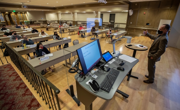 A masked professor teaches a class of masked, socially distanced students