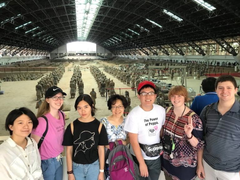 A group of people stand on a balcony overlooking Chinese terra-cotta warriors.