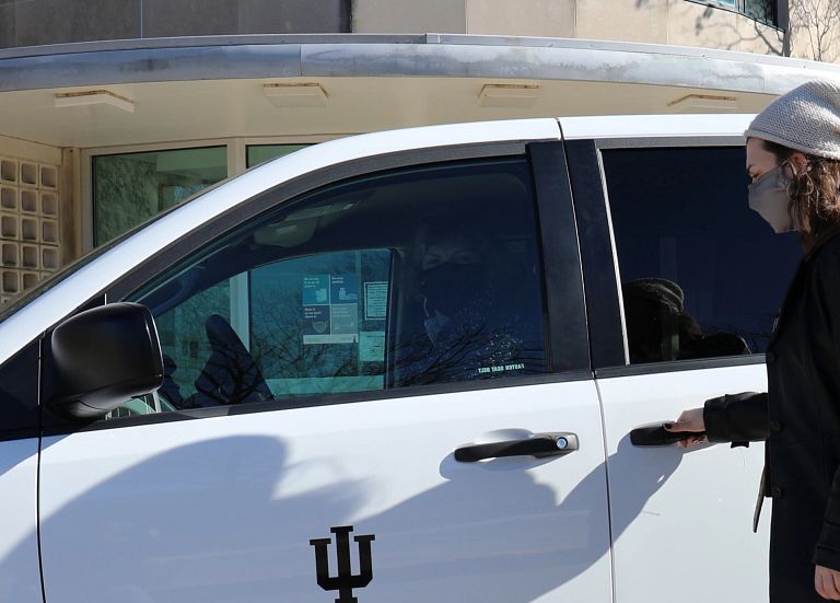 A masked woman opens the door of an IU Ride minivan