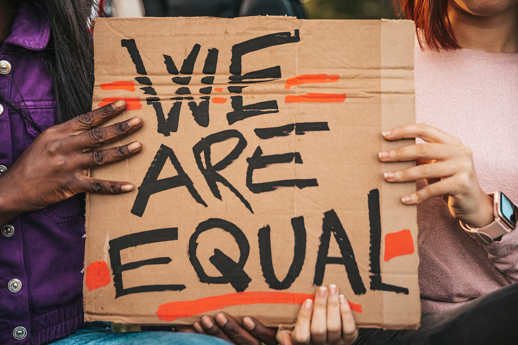 Two hands hold a sign that reads we are equal