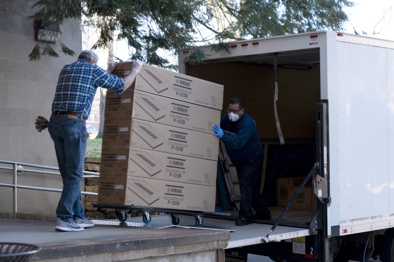 Two men unload boxes of digital keyboards from a truck