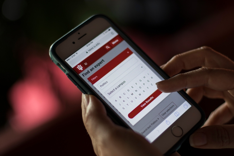 Hands hold a phone displaying the IU Experts Database.