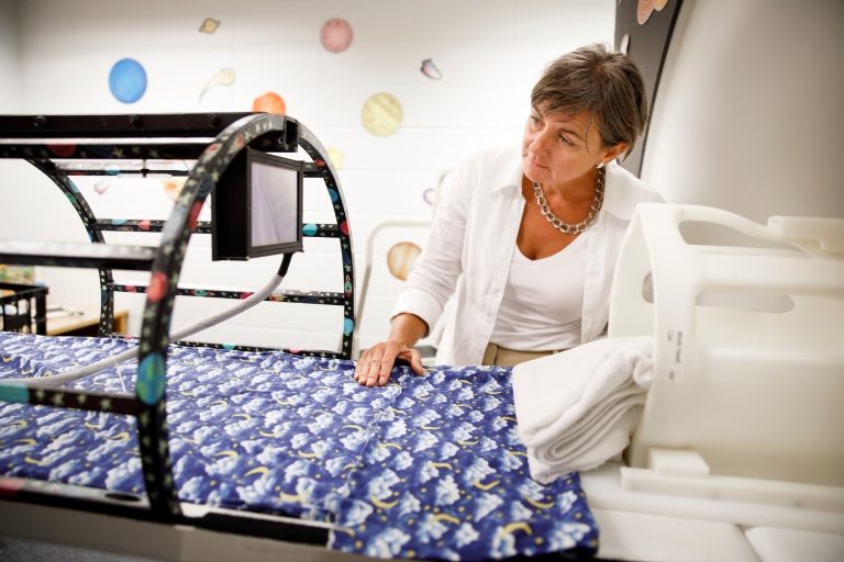 Karin James sets up a tablet, center left, outside of a MRI simulator.