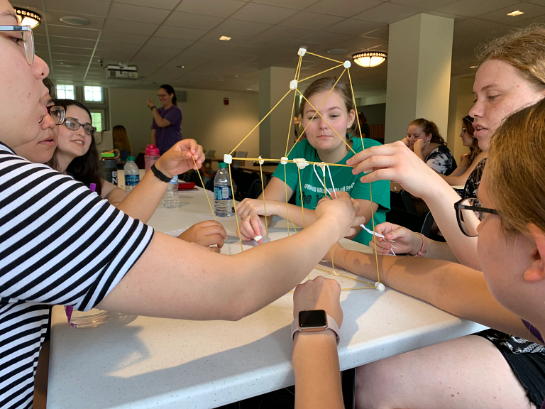 Several female students make a spaghetti tower