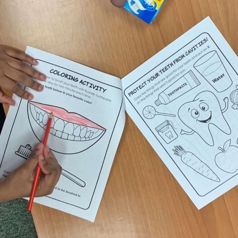 A child colors a coloring book with pictures of mouths and teeth