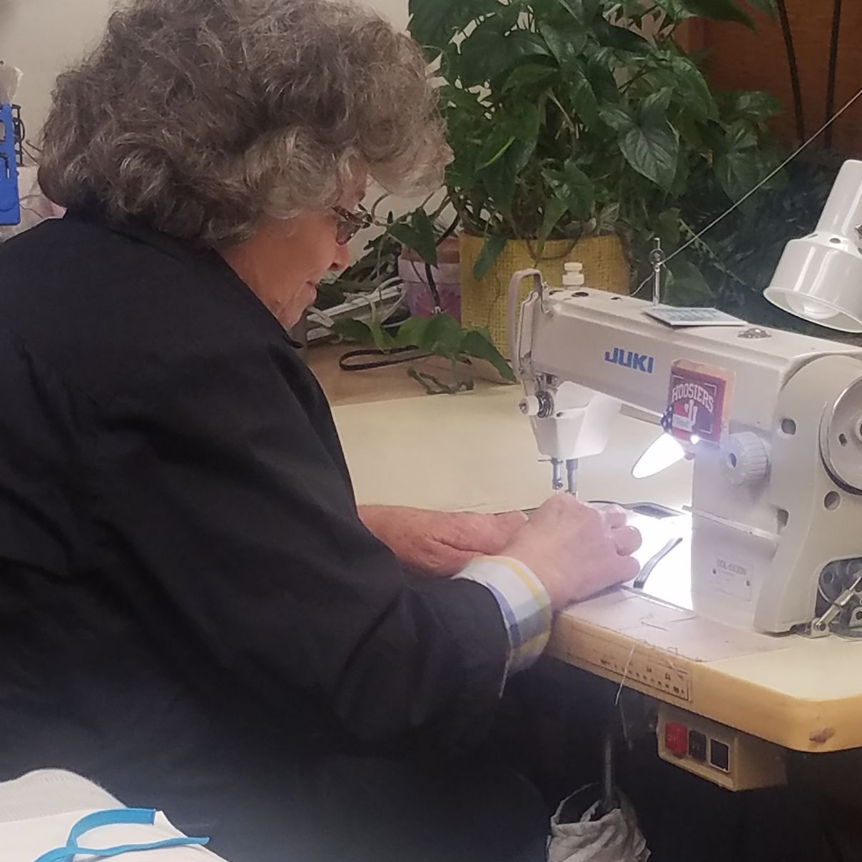 A woman sits at a sewing machine, making masks.