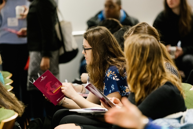 A student looks at a program booklet while sitting in a crowded auditorium