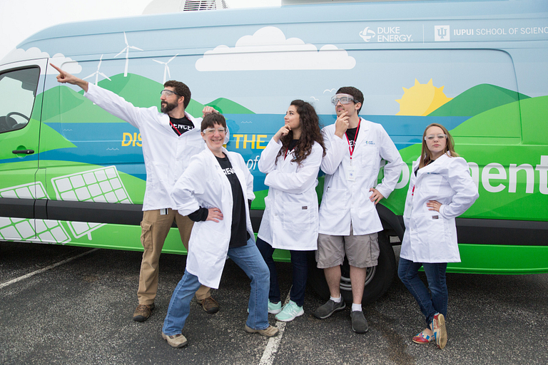 A group of science educators in lab coats stand in front of the mobile lab.