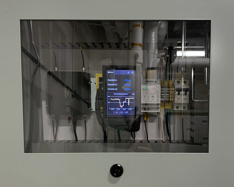 An energy monitor inside a gray metal box with a glass front