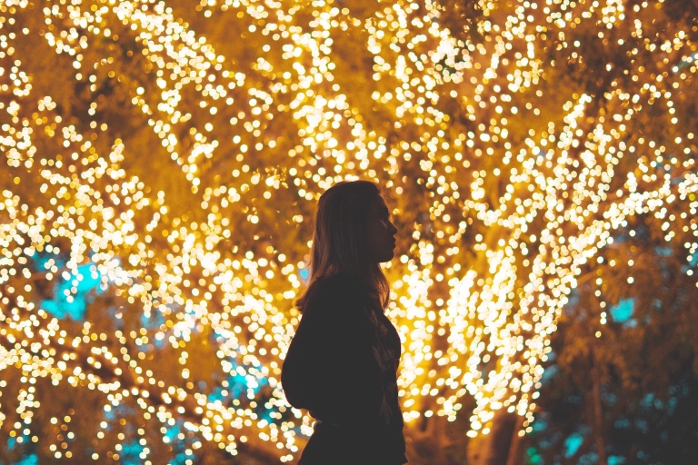 Lit-up tree outside at night with person walking in front of it.