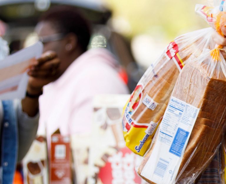 A woman wearing a mask gathers loaves of bread from a grocery cart.