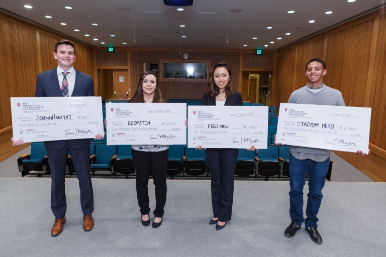 Four students stand with giant checks