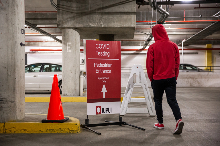 Student walks past a COVID-19 testing sign in a parking garage