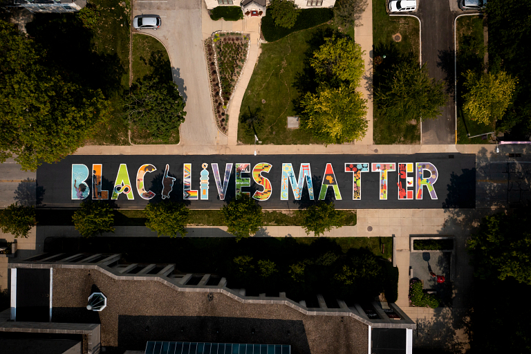 A colorful mural reading 'Black Lives Matter' is displayed on the black pavement of Jordan Avenue