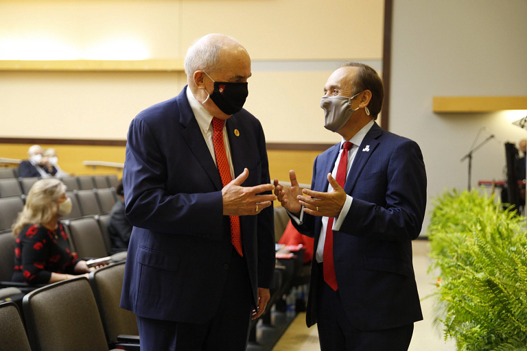 Michael A. McRobbie and Nasser H. Paydar wearing masks and having a conversation in an auditorium