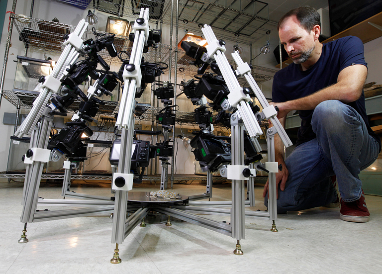 A man kneels next to an array of cameras.