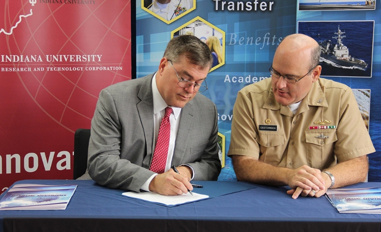 Fred Cate of IU signs a document while Capt. Mark Oesterreich of NSWC Crane watches.