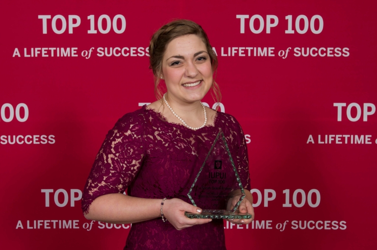 IUPUI's Sarah Grace Fraser stands holding her trophy for Top 100 Most Outstanding Student.