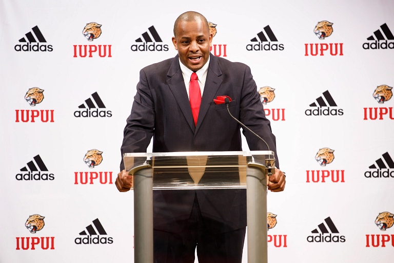 New IUPUI men's basketball coach Matt Crenshaw speaking at a podium.