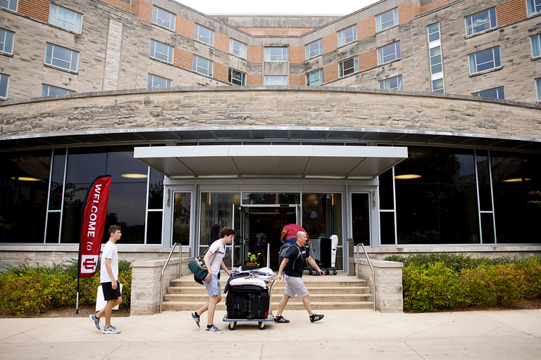 Students pushing luggage across a sidewalk during move in