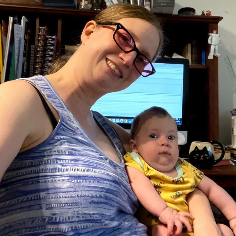 A woman holds her child while sitting in front of a computer.