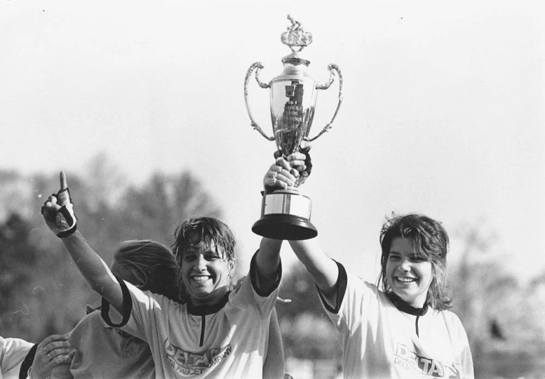 Two cyclists celebrate and hold up a large trophy.