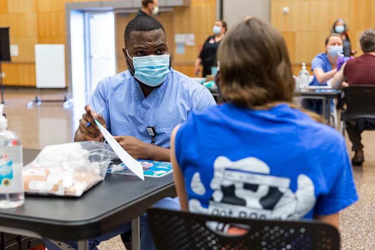 A student sits with sleeve rolled up waiting to receive a COVID-19 vaccine.