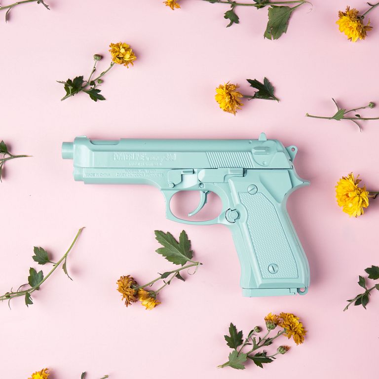 A teal colored gun on a pink background with flowers strewn about