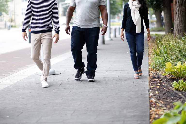 Three people pictured from the torso down walk side-by-side on a pedestrian trail