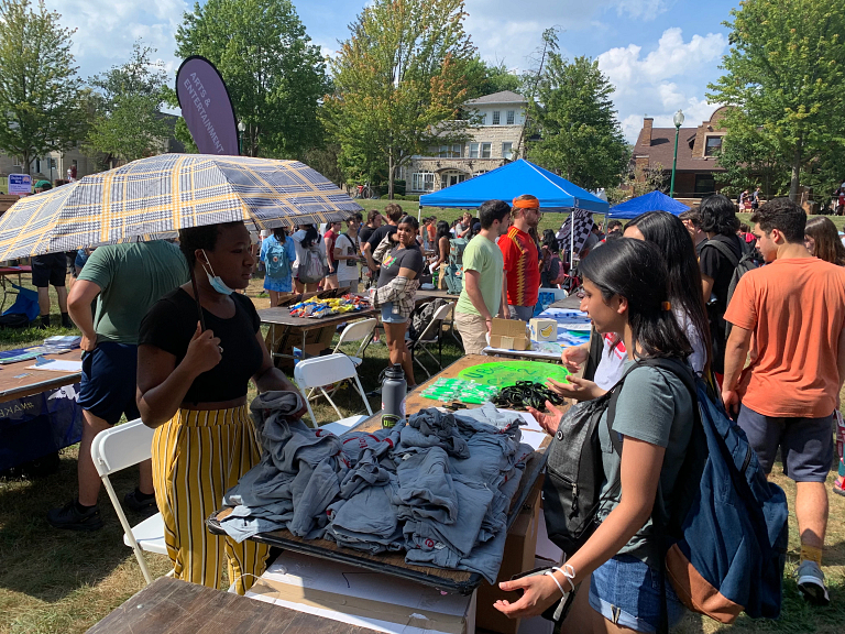 A woman holding an umbrella and hosting a table with T-shirts talks to two other women