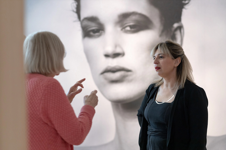 Two women having a conversation in front of a mural-sized black and white photo on the wall.