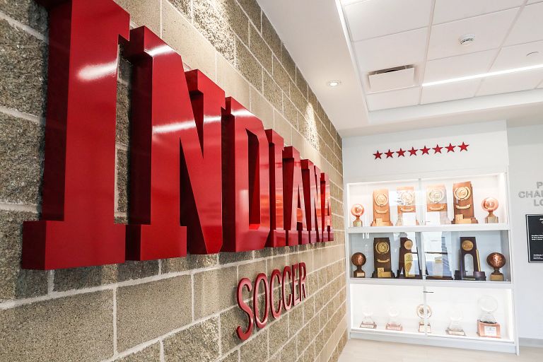 Red letters spelling Indiana soccer hang on a wall next to a trophy case.