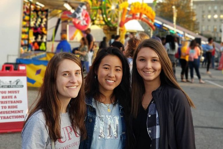 Three students smile at a carnival.