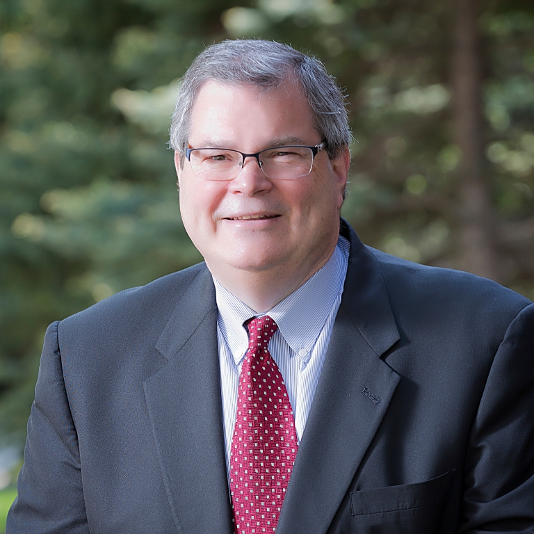 A photo of Paul Halverson in a suit and red tie, wearing glasses