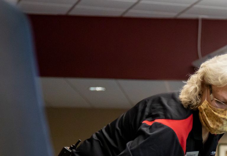 A woman wearing a mask cleans a computer lab table