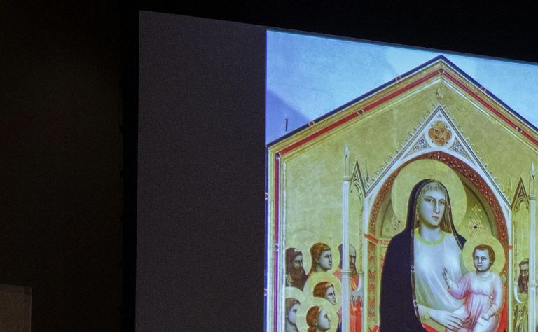 A professor shows a class slides of paintings in a darkened classroom
