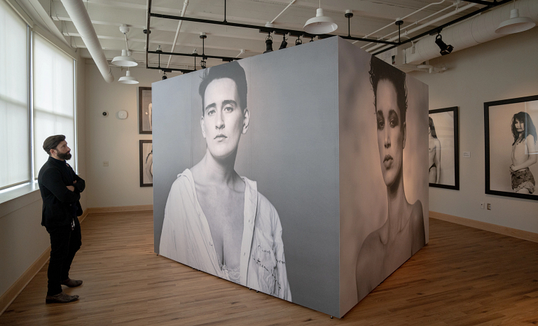 A man in a suit stands and looks at a mural-sized photograph of an androgynous model.