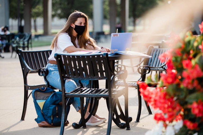 a woman sits at table outdoors on her laptop