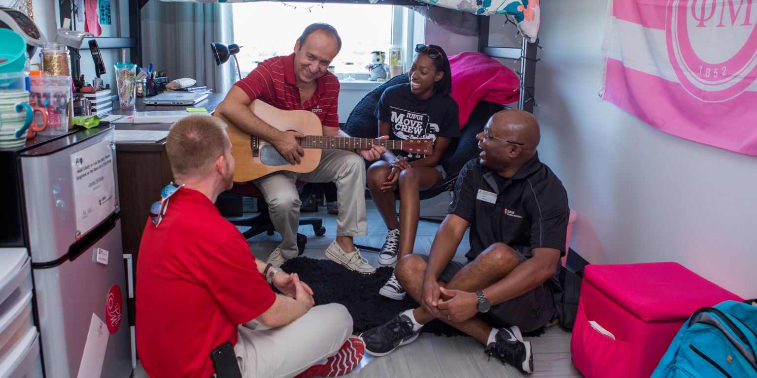 IUPUI Chancellor Nasser Paydar plays guitar for some students and staff members in a dorm room