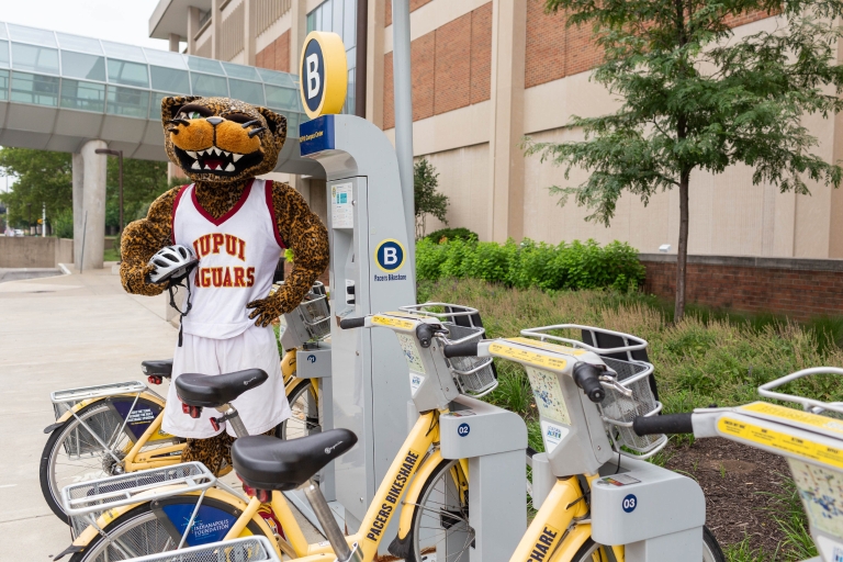 A Jaguar mascot stands by a rack of Pacers Bikeshare bicycles.