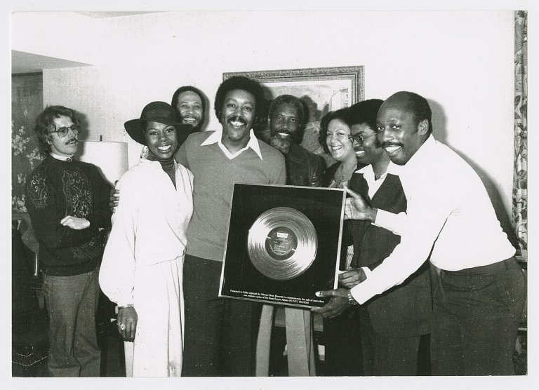 Group of people smile while holding gold record