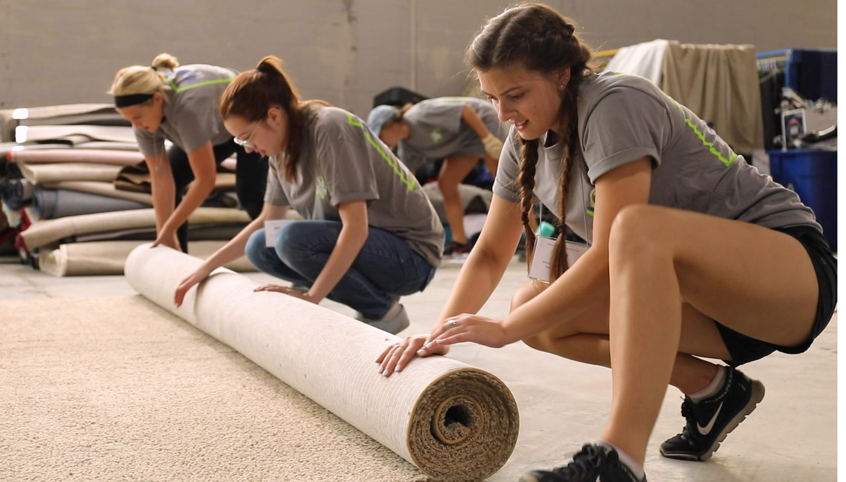 Three female students roll up a section of carpet.