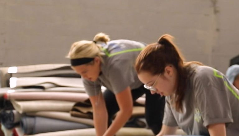 Three female students roll up a section of carpet.