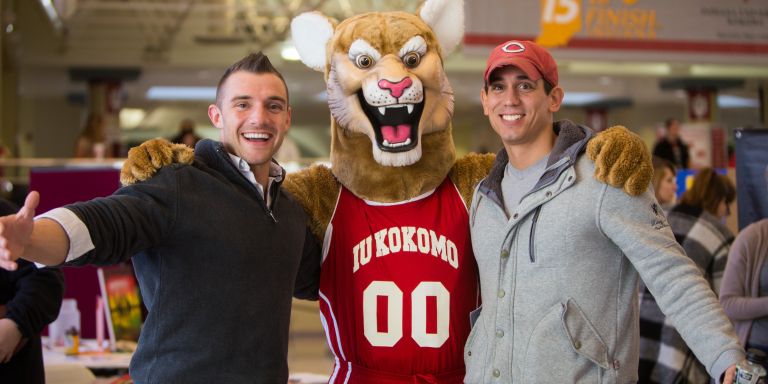 IU Kokomo's Kingston Cougar mascot stands with arms around two male students.