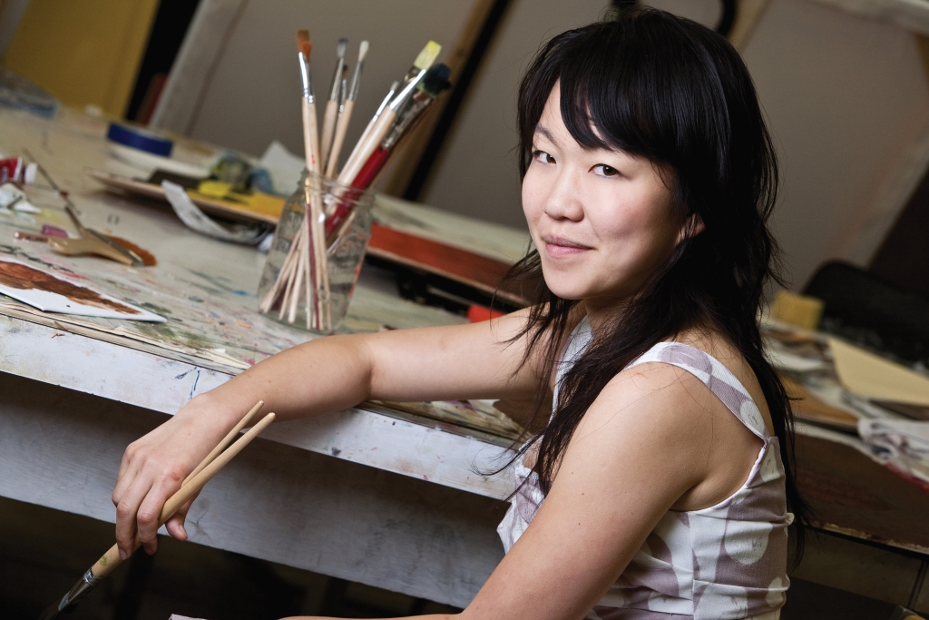 Ann Kim holding a paint brush in her hand in front of a painting table