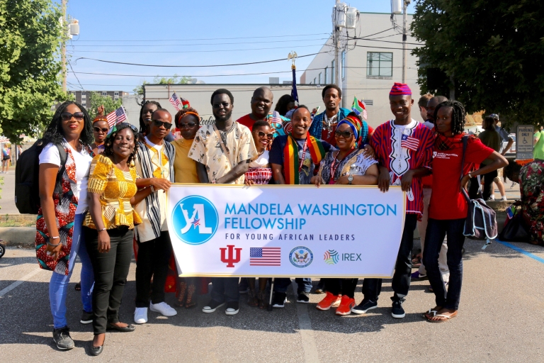 A group of Mandela Fellows hold a banner with the program's name and logos for the partners.