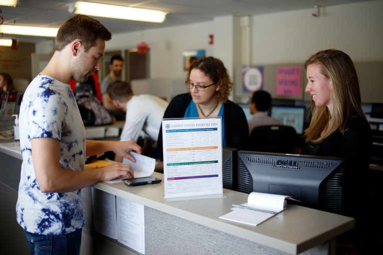 Student standing at a counter is assisted by two IU staff members in the passport office. 